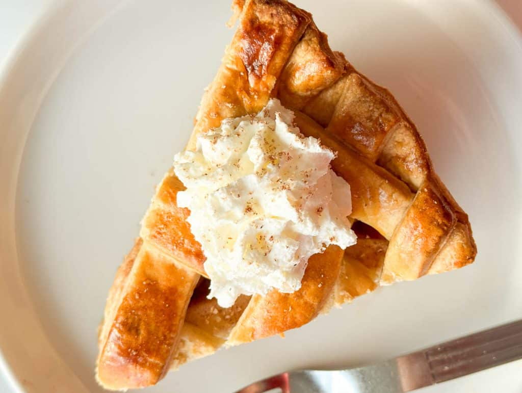Apple pie slice topped with whipped cream on a white plate.