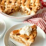 Apple pie with a plated slice beside it on a striped towel.
