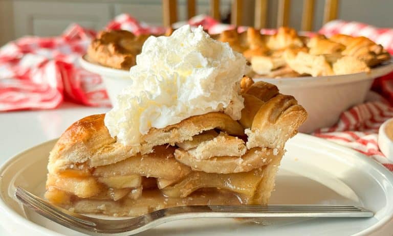 Apple pie slice topped with whipped cream on a white plate.
