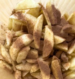 Bowl of sliced apples coated with cinnamon and sugar.
