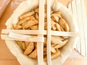 Apple pie filled with cinnamon apples and the first dough strips laid across the top.