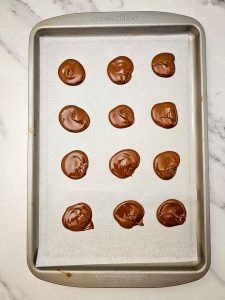 Spoonfuls of melted chocolate arranged in rows on a parchment-lined baking sheet.