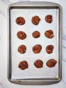 Chocolate rounds topped with pecan halves on a parchment-lined baking sheet.