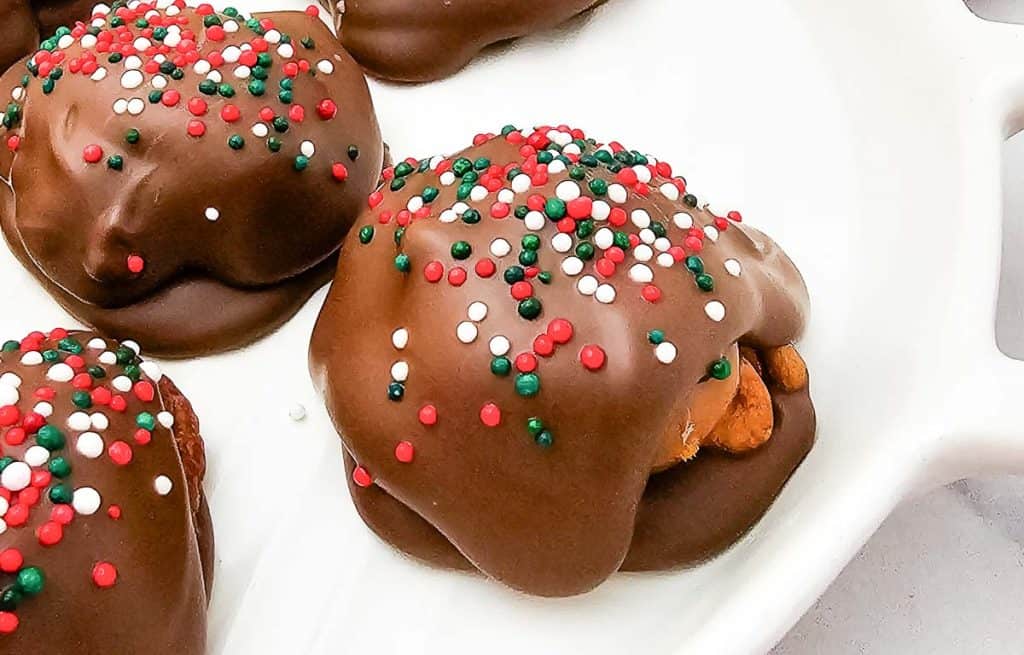 Close-up of a chocolate-covered caramel pecan cluster with red, green, and white sprinkles.