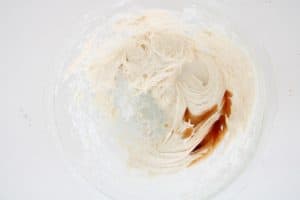 Partially mixed frosting with vanilla extract pooling on the side, ready to blend.