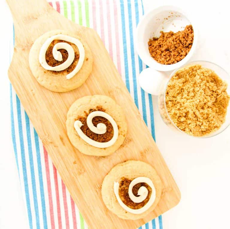 Top-down view of cinnamon swirl cookies on a wooden board with bowls of brown sugar nearby.