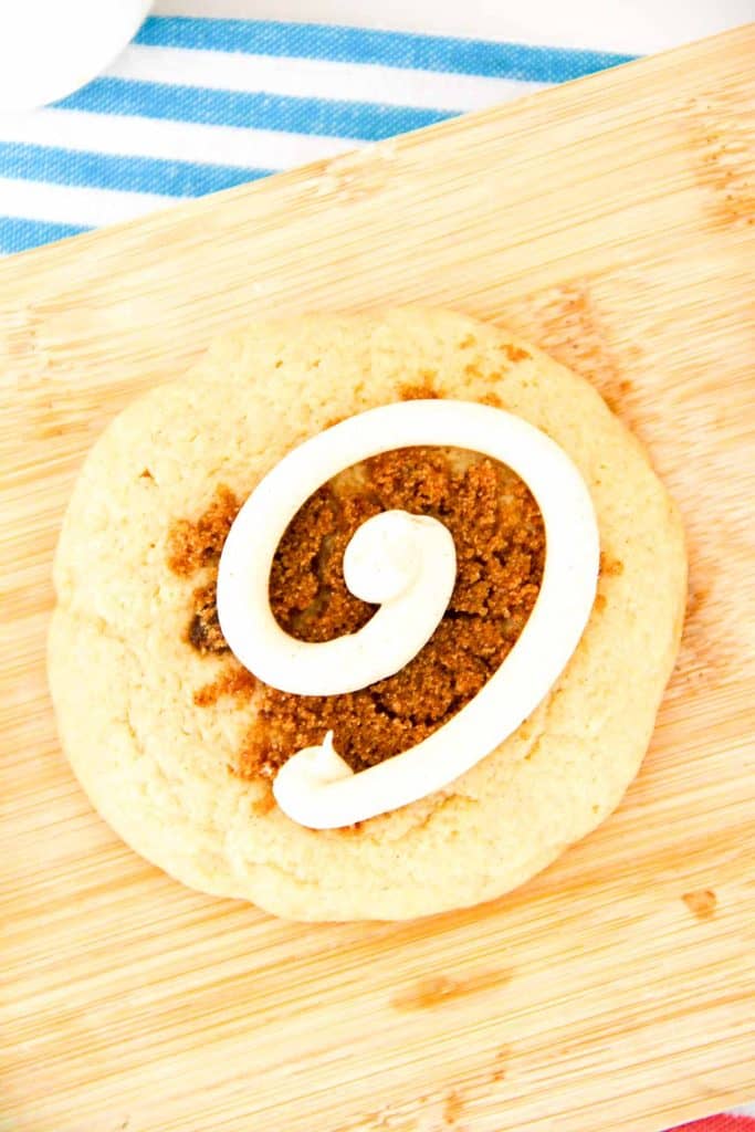 A single cinnamon swirl cookie topped with a neat white frosting spiral on a wooden board.