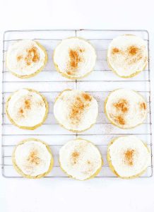 Frosted eggnog cookies cooling on a wire rack with cinnamon sprinkled on top.