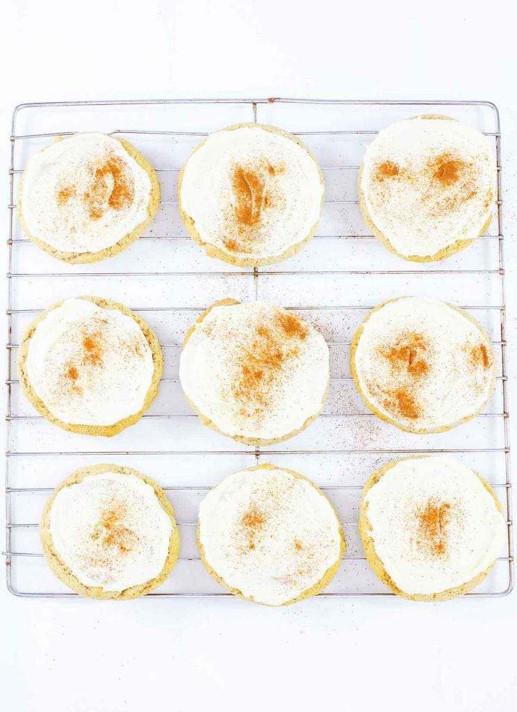 Frosted eggnog cookies cooling on a wire rack with cinnamon sprinkled on top.