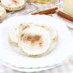 Eggnog cookies on a plate with cinnamon sticks and a glass of eggnog in the background.