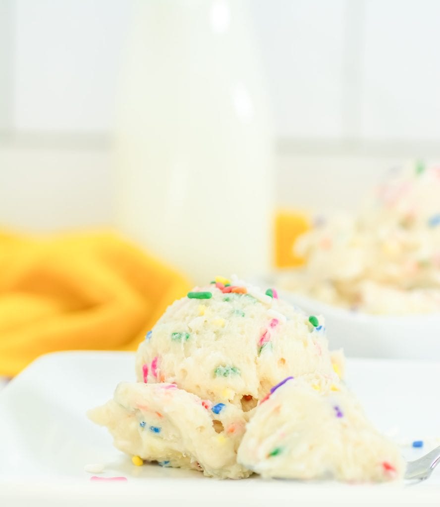 Scoop of Funfetti cookie dough on a white plate with scattered sprinkles and a spoon beside it.