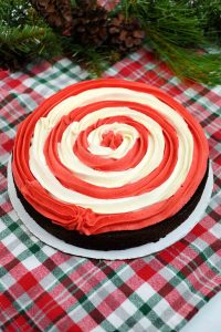 Chocolate cake topped with red and white swirl frosting on a holiday tablecloth.