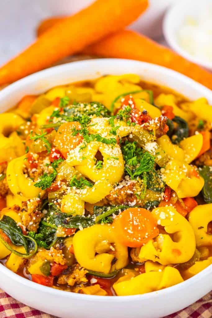 Close-up of tortellini soup highlighting pasta rings and sausage pieces.