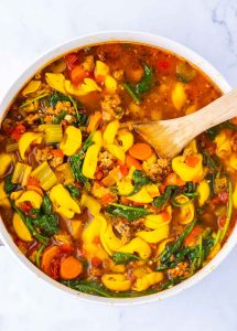 Tortellini soup simmering in a pot with vegetables and sausage.