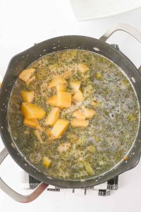 Pot filled with broth, herbs, and diced potatoes simmering.