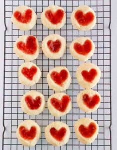 Baked cookies on a cooling rack, showing heart-shaped jam centers.