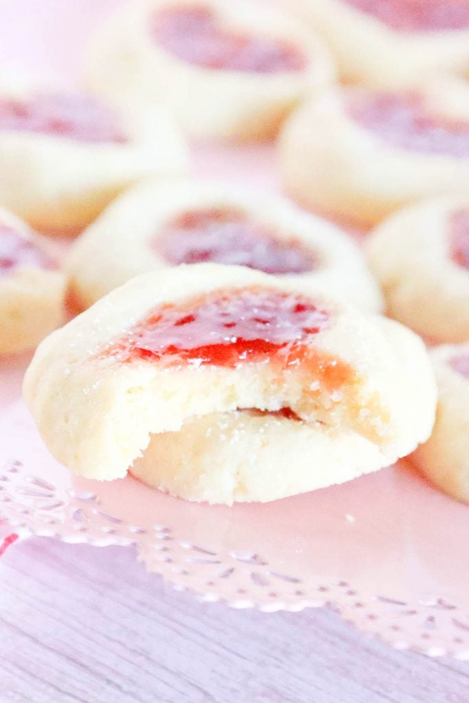 Heart thumbprint cookie with a bite taken out, showing soft texture and jam center.