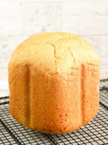 Loaf of white bread from a bread machine cooling on a wire rack.