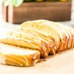 Sliced lemon loaf with glaze on wooden board.
