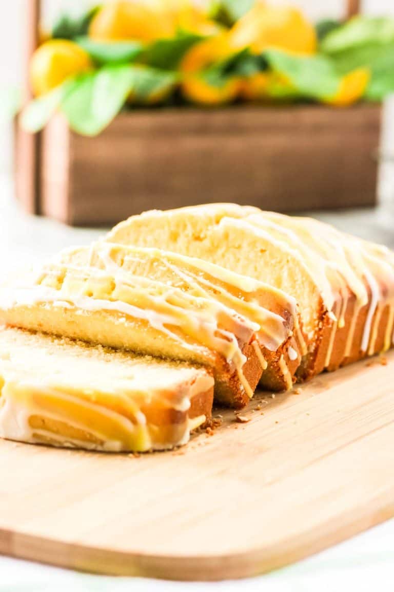 Sliced lemon loaf with glaze on wooden board.