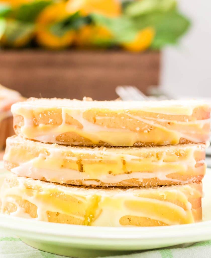 Stacked lemon loaf slices on plate with plates and forks in background.
