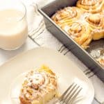 Cinnamon roll served on a plate with a glass of milk nearby.