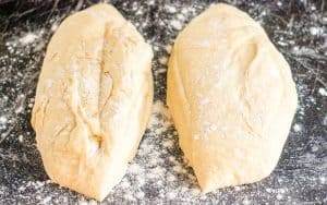 Two portions of dough resting on a floured work surface, ready for shaping.