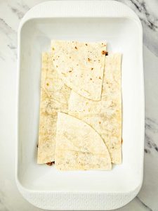 Flour tortillas layered over enchilada casserole filling in a baking dish.