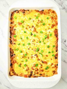 Baked enchilada casserole topped with chopped green onions in a baking dish.