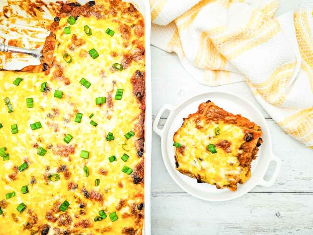 Baked enchilada casserole topped with chopped green onions in a baking dish.