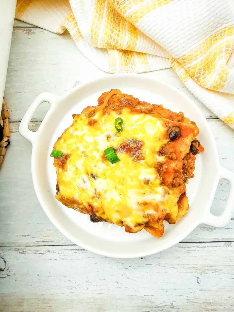 Slice of enchilada casserole with melted cheese and green onions on a white plate.