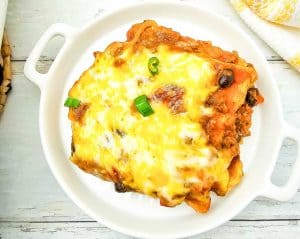 Enchilada casserole slice with melted cheese and green onions served on a white plate.