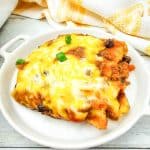Enchilada casserole slice with melted cheese and green onions served on a white plate.