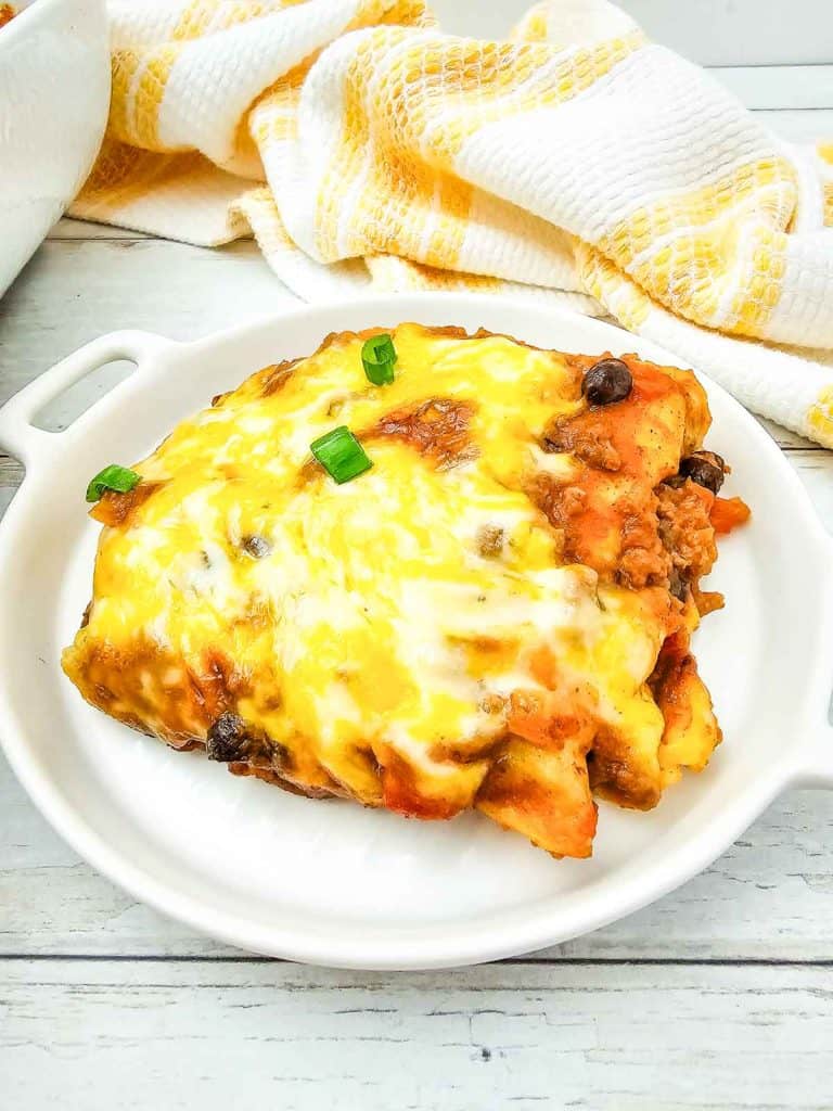 Enchilada casserole slice with melted cheese and green onions served on a white plate.