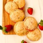 Strawberry cream cheese hand pies arranged on a wooden serving board surrounded by fresh strawberries.