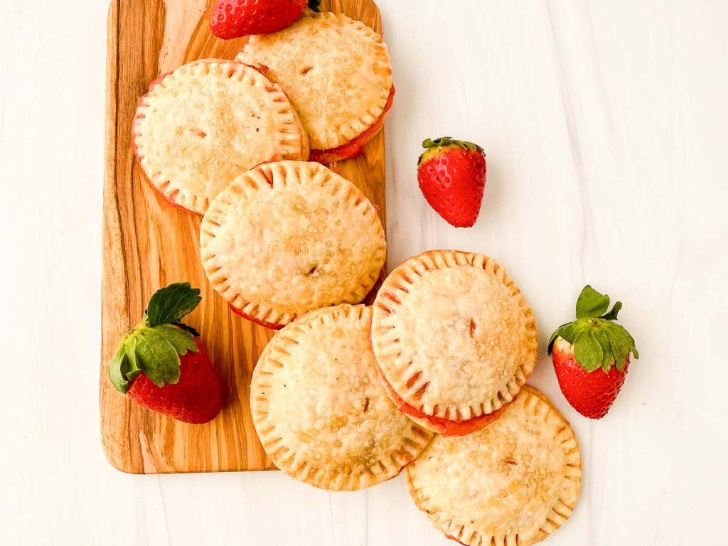 Several baked strawberry cream cheese hand pies with golden tops and crimped edges on a wooden board.