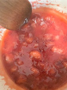 Wooden spoon stirring chunky strawberry filling in a pot, showing pieces of strawberries in a glossy red sauce.