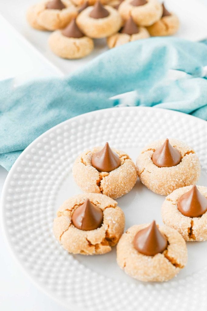 Close-up of peanut butter blossom cookies on a plate with more cookies blurred in the background.