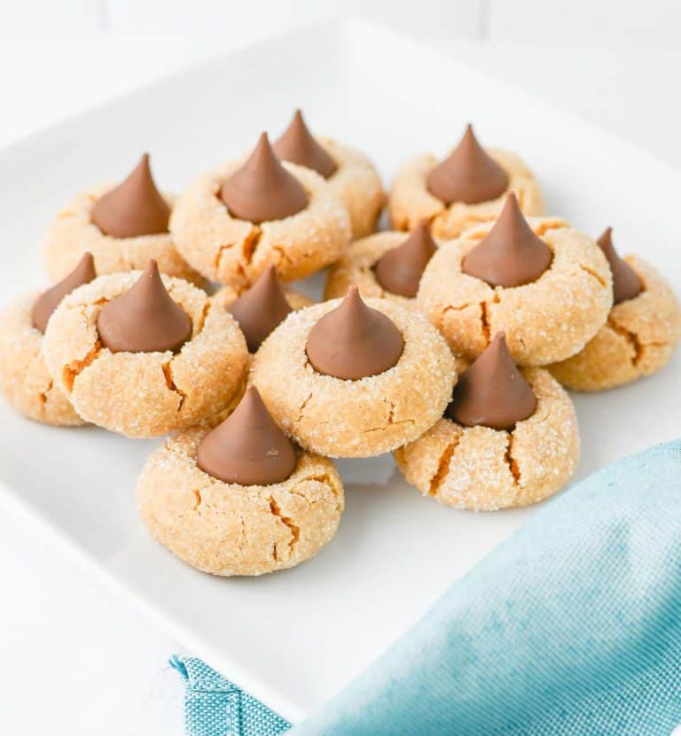 Close-up of peanut butter blossom cookies topped with chocolate kisses on a white plate, with a blue cloth nearby.