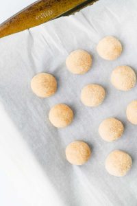 Small sugar-coated dough balls spaced on a parchment-lined baking sheet.
