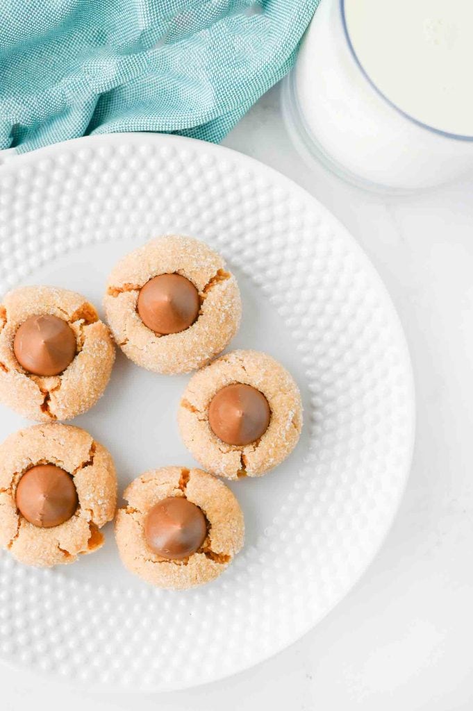 Overhead view of peanut butter blossom cookies on a plate with a glass of milk and blue napkin.