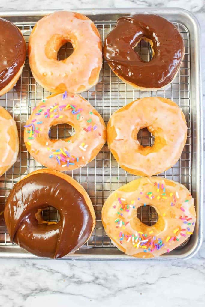 Assorted donuts with chocolate glaze, vanilla glaze, and colorful sprinkles on a cooling rack.