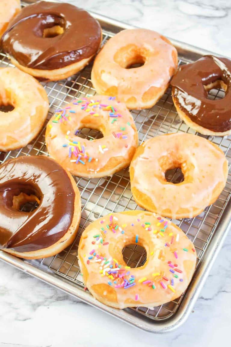 Tray of glazed and chocolate-covered donuts with a few topped with rainbow sprinkles.