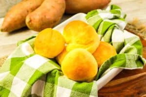 Freshly baked sweet potato rolls in a bowl lined with a green checkered cloth.
