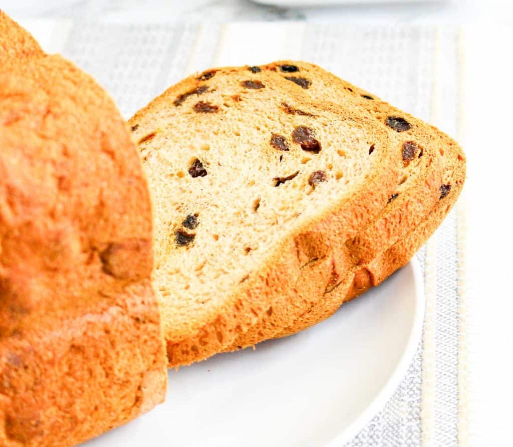 Fresh loaf of cinnamon raisin bread with two slices laid in front on a plate.