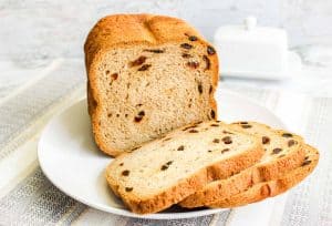 Sliced cinnamon raisin bread on a white plate with a loaf in the background.