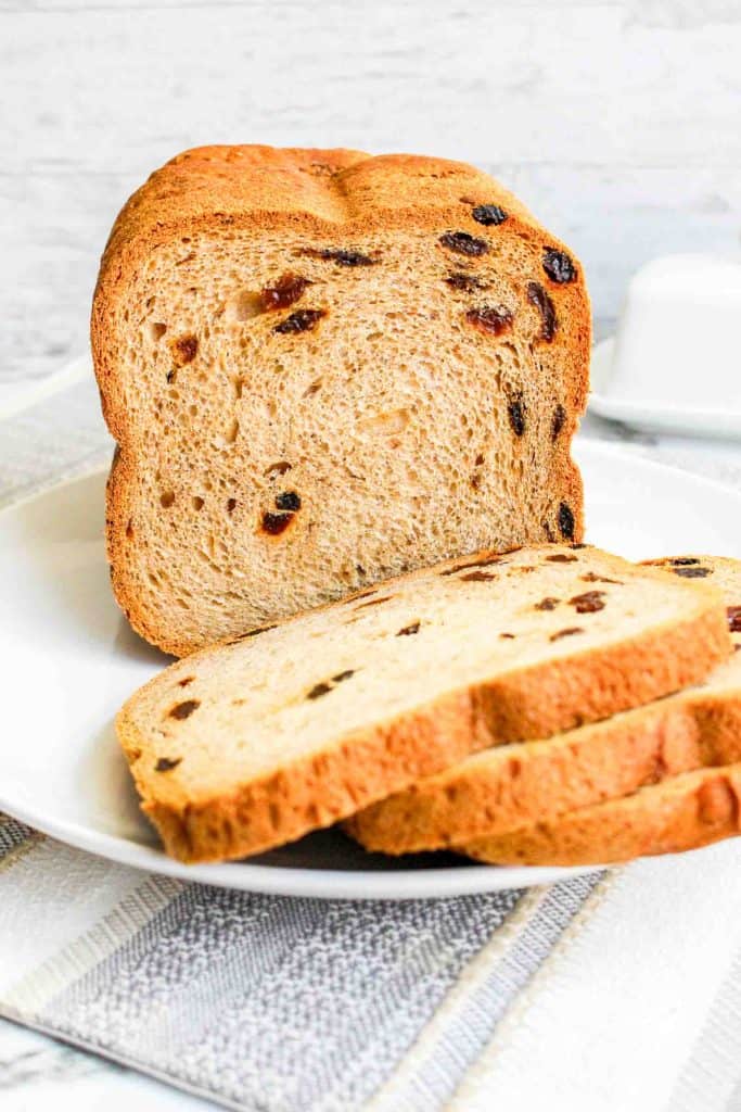 Fresh loaf of cinnamon raisin bread with two slices laid in front on a plate.