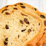 Close view of a loaf of cinnamon raisin bread with slices showing raisins inside.