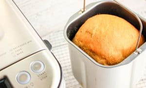 Baked loaf of bread inside a bread machine pan, golden brown on top.
