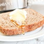 Honey dripping from a buttered slice of honey wheat bread on a white plate.